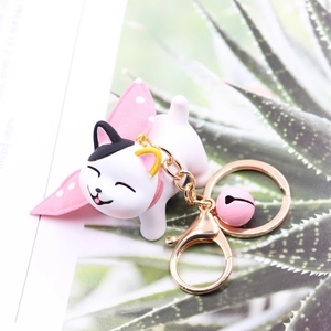 Detail of cute white resin cat keychain with pink bell and gold metal hardware