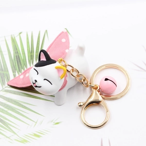 Cute white resin cat keychain with pink polka dot bow and golden bell on white background