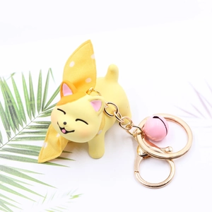 Cute yellow cartoon cat keychain with pink bell and bow on a clean white background