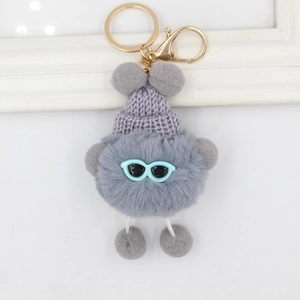 Détail d'un porte-clés monstre en peluche grise avec un bonnet tricoté et lunettes bleues
