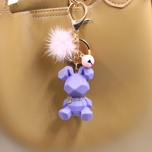 Détail de l'ours géométrique violet avec pompon rose et grelot sur un sac en cuir marron