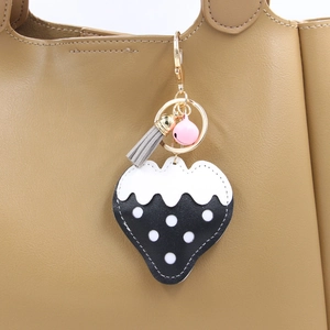 Détail du porte-clés fraise à pois avec clochette rose et pompon gris sur un sac en cuir