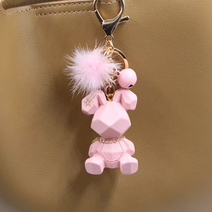 Détail d'un porte-clés lapin géométrique rose avec pompon en peluche et clochette sur un sac