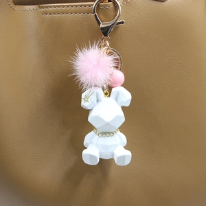 Détail du pendentif lapin géométrique blanc avec pompon rose sur un sac en cuir marron