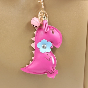 Cute pink PU leather dinosaur keychain with tassel and bell charm on a khaki leather bag