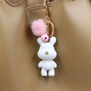 Detail eines gestrickten weißen Hasen-Anhängers mit rosa Fellball an einer Ledertasche