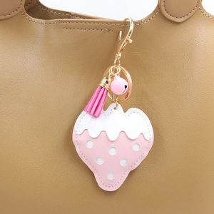 Porte-clés fraise rose avec pompon et clochette sur un sac à main en cuir marron