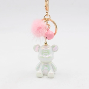 Detail of pearlescent white resin bear keychain with pink fur pompom and golden bell