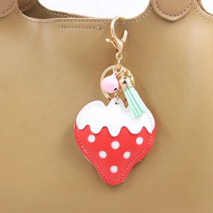 Détail d'un porte-clés fraise avec pompon et clochette sur un sac en cuir brun