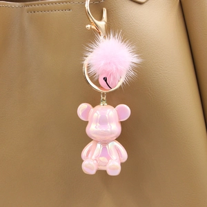 Close-up of pink pearlescent bear keychain with fluffy fur pompom on a leather bag