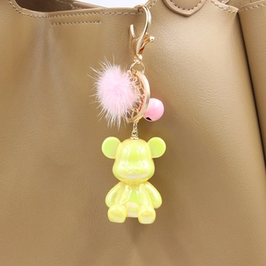 Detail of yellow pearlescent bear charm with pink fur ball and bell on a leather bag