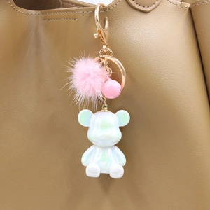 Close-up of pearl white resin bear keychain with pink fur pompom on a leather bag