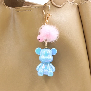 Detail of blue pearl resin bear keychain with pink faux fur ball on a beige leather handbag