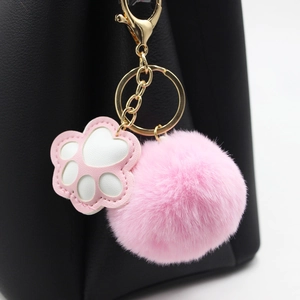 Nahaufnahme von rosa Katzenpfoten-Anhänger und flauschigem Fellbommel an schwarzer Tasche