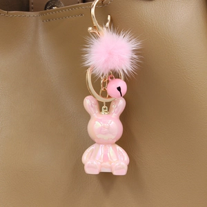 Detailed shot of pink resin rabbit keychain with plush ball and gold bell on a handbag
