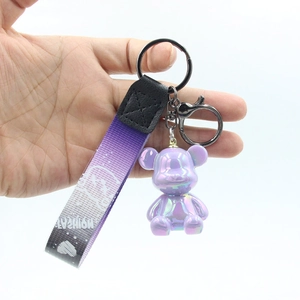 Detail shot of a gradient bear keychain with purple ribbon held in hand on white background