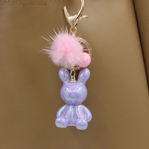 Detailed view of iridescent purple rabbit keychain with pink fur pom pom on brown leather bag