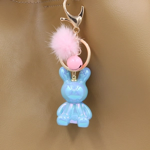 Iridescent blue rabbit keychain with pink fur pompom on a brown leather handbag detail