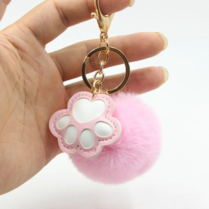 Nahaufnahme von flauschigem rosa Kunstfell-Bommel und Katzenpfote mit goldenem Verschluss