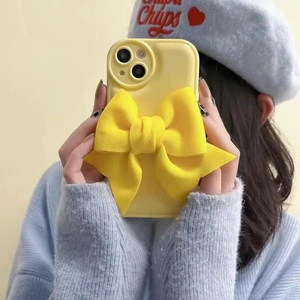Detail of a bright yellow fabric phone case featuring a large puffy 3D bow decoration