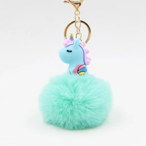 Détail d'un pompon vert menthe en fausse fourrure avec un charme licorne en silicone bleu