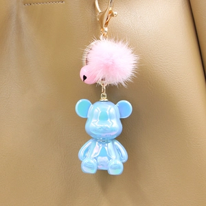 Blue pearlescent bear keychain with pink fur pompom and heart bell on khaki handbag
