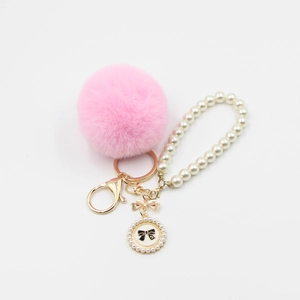 Detailed macro view of pink faux fur pompom keychain with gold bow and pearl wristlet