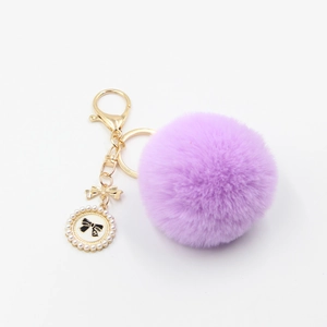 Detail of lavender faux fur pom pom keychain with gold bow and pearl perfume charm