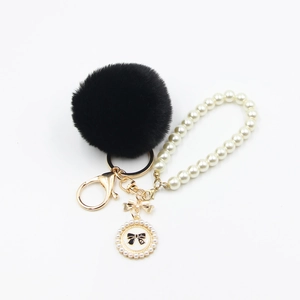 Detail of black faux fur pompom keychain with pearl chain and number five pendant