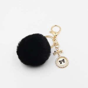 Detailed view of black faux fur pompom keychain with golden bow and pearl charm