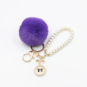 Detail view of purple faux fur pompom keychain with cream pearl strap and bow pendant