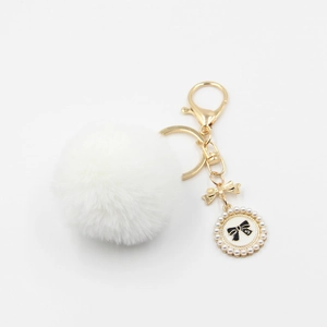 Detail of white fluffy pompom keychain with golden bow and pearl enamel pendant charm
