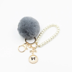 Detailed macro view of the grey faux fur pompom and cream pearl chain keychain accessory