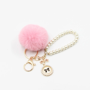 Close-up of pink fluffy fur pompom with pearl strap and gold clasp bag accessory