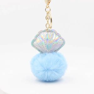 Macro detail of sky blue pompom and iridescent silver shell keychain with gold metal clasp