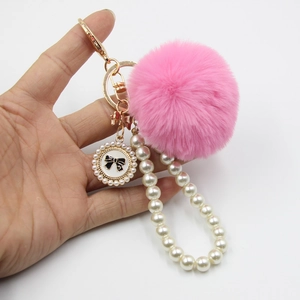 Detailed view of pink fluffy pompom keychain with white pearl chain and black bow pendant