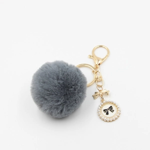 Detail view of gray pompom keychain with golden bow and pearl perfume charm