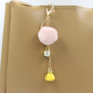 Dettaglio portachiavi con pompon rosa, campanellino dorato e nappa su una borsa