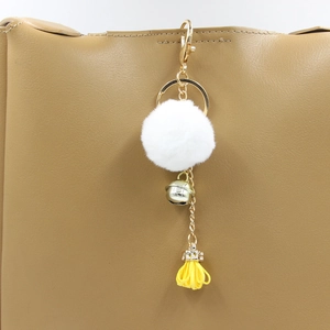 Dettaglio di un portachiavi a pompon in pelliccia sintetica bianca con campanello d'oro