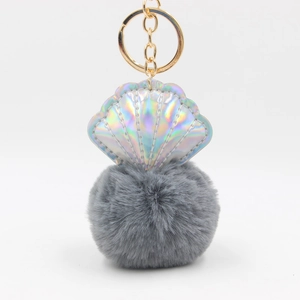 Detail of laser shell keychain with golden ring and soft grey faux fur pom pom charm