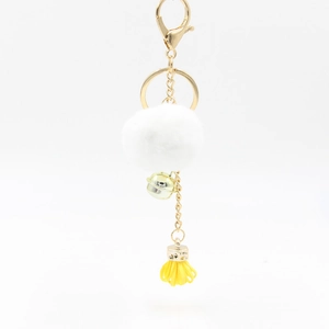 Dettaglio portachiavi a pompon bianco con campanellino dorato e nappa giallo brillante