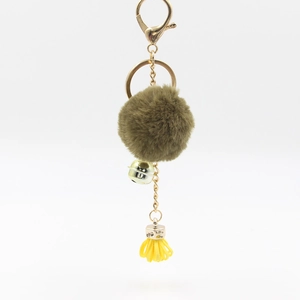 Dettaglio portachiavi di peluche con pompon verde, chiusura dorata e nappa gialla