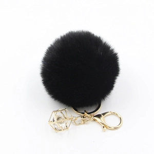 Macro detail of black faux fur pompom keychain with golden crystal geometric charm