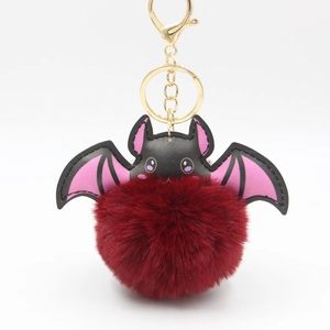 Detail of burgundy plush ball keychain with black and pink leather bat wings and gold clasp
