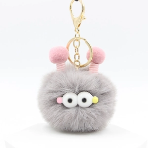 Dettaglio del portachiavi mostro in peluche grigio con pelliccia morbida e pompon rosa