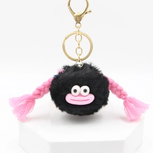 Detail view of a black fluffy monster keychain with pink braids and big eyes on white base