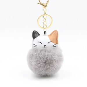 Close-up of fluffy grey pompom and cute cat faux leather keychain with golden clasp
