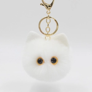 Detail of white plush cat keychain with fluffy texture, yellow eyes, and gold metal clip