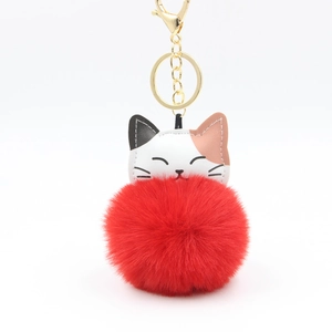 Detail of red plush ball keychain featuring a cute leather cat head and gold hardware