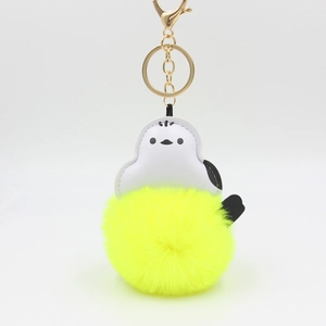 Detail of penguin plush keychain with gold lobster clasp and bright yellow faux fur ball